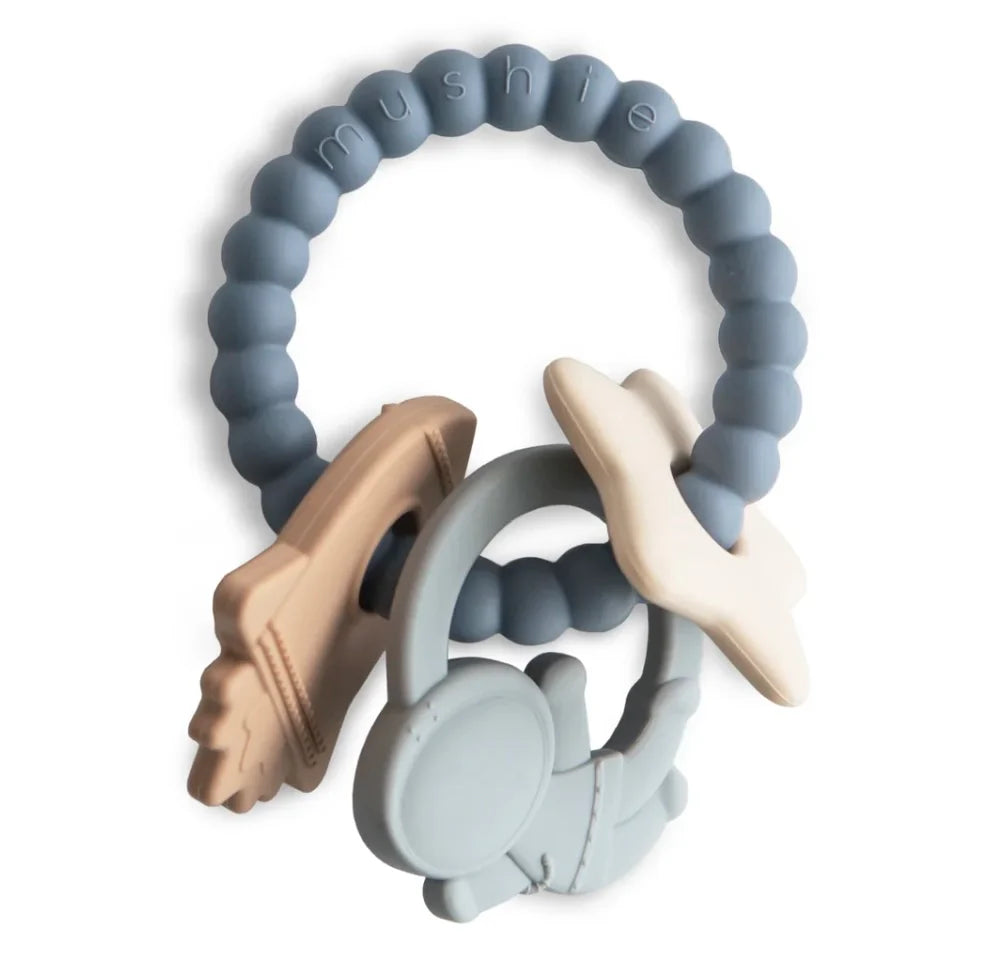 Astronauten Beißring von Mushie: Ring aus silikon mit Rakete, Stern und Astronauten Anhänger aus silikon dran.