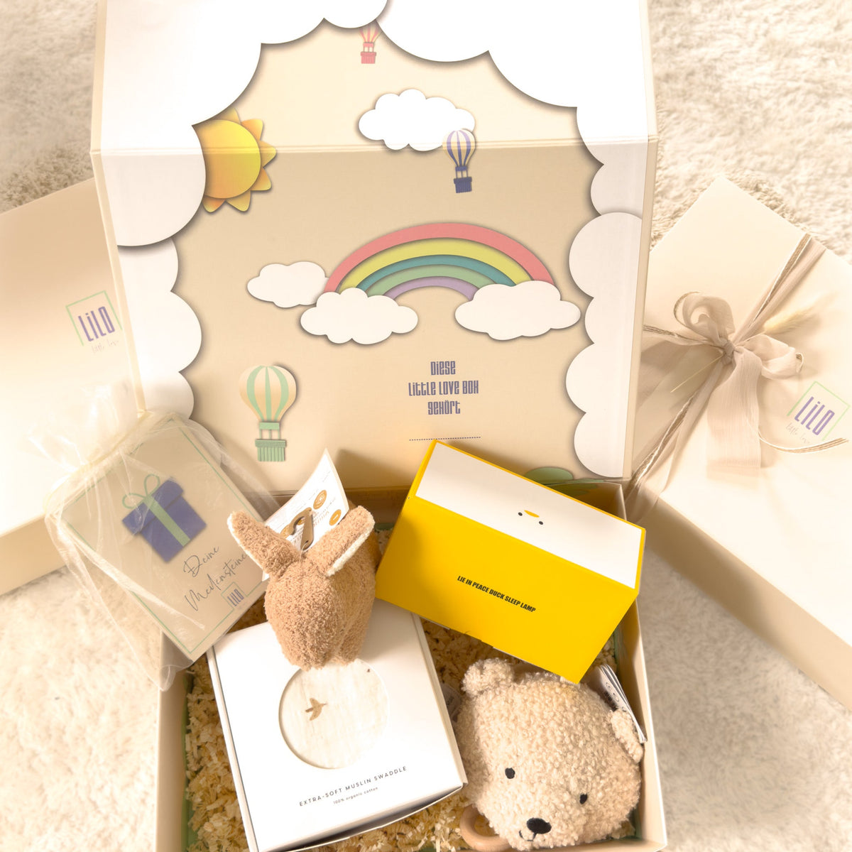 Geschenkbox für Neugeborene in Beige von lilo.littlelove mit Meilensteinkarten, Hasenrassel, Nachtlicht, Teddy-Spieluhr und Puckdecke – liebevoll verpackt in hochwertiger Erinnerungsbox mit Regenbogenmotiv