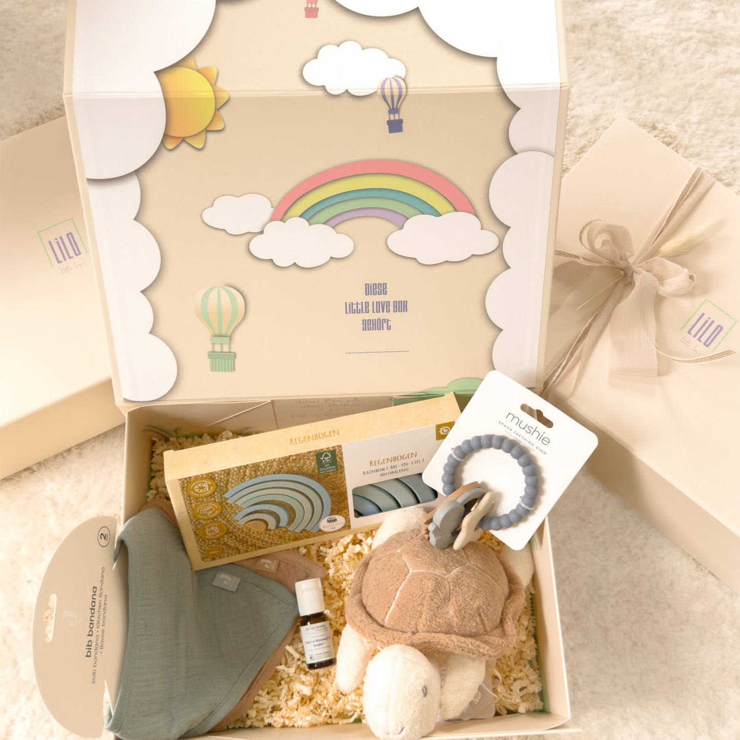 lilo little love Babygeschenkbox in beige mit Regenbogen motiv. gefüllt mit Bandanas, Schildkröte als Kuscheltier, Fenchel-kümmel Öl, blauer Regenbogen aus Holz zum spielen und ein blauer astronautenbeißring. Babygeschenk für jungs. 