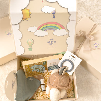 lilo little love Babygeschenkbox in beige mit Regenbogen motiv. gefüllt mit Bandanas, Schildkröte als Kuscheltier, Fenchel-kümmel Öl, blauer Regenbogen aus Holz zum spielen und ein blauer astronautenbeißring. Babygeschenk für jungs. 