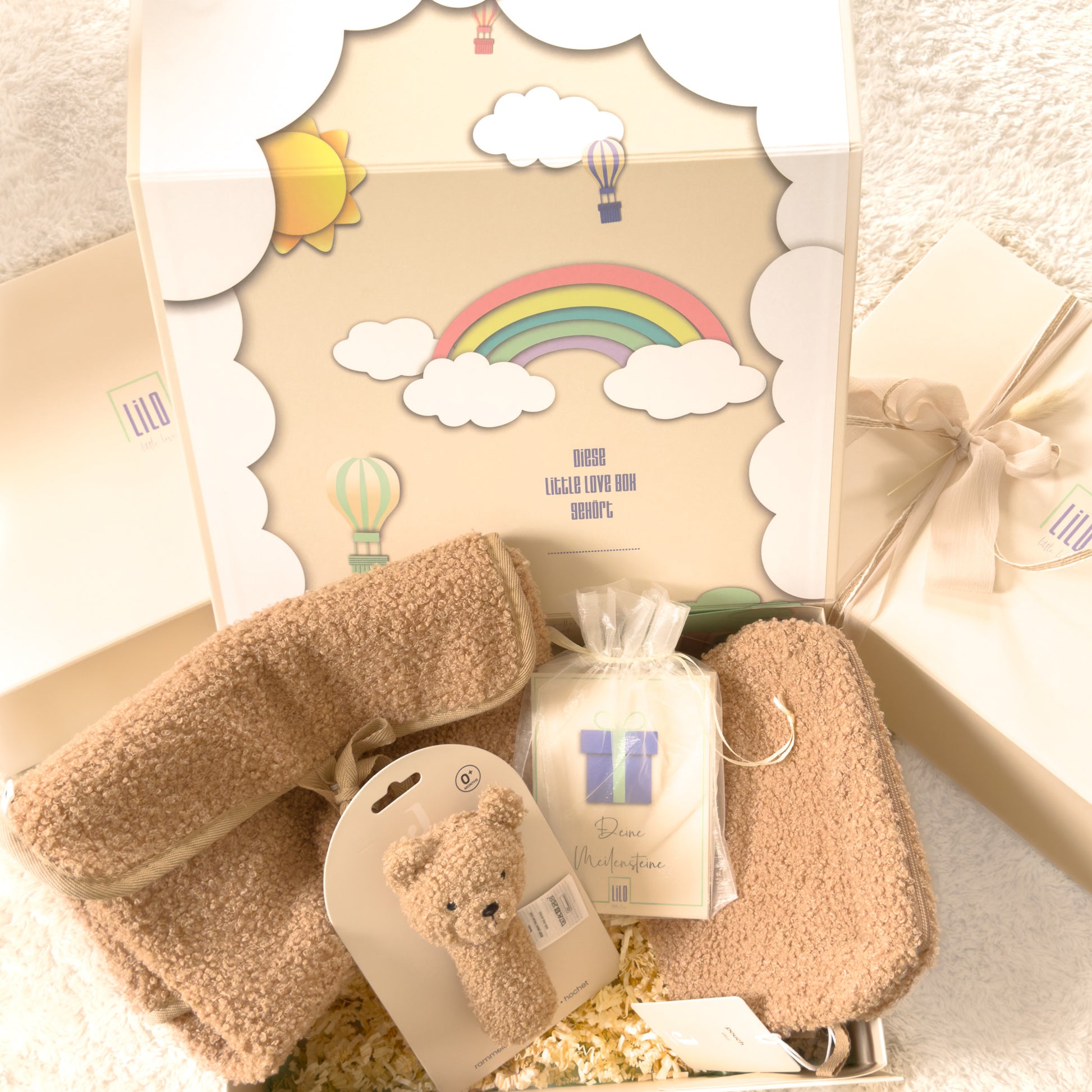 Geschenkbox für Neugeborene in Beige von lilo.littlelove mit Teddy-Rassel, Windelbeutel, Wickeltasche und Meilensteinkarten – liebevoll verpackt in hochwertiger Erinnerungsbox mit Regenbogenmotiv
