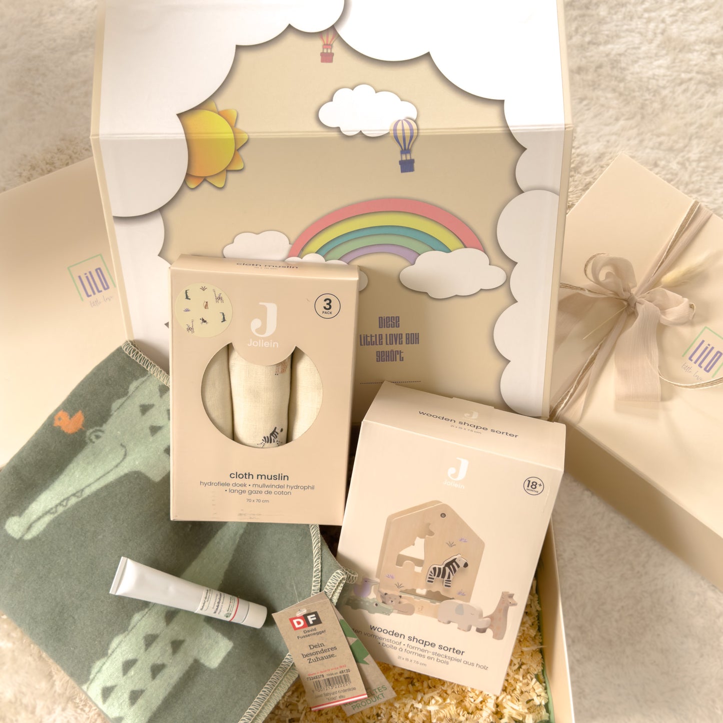 Babygeschenkbox von lilo little love gefüllt mit einer babydecke mit Krokodilmotiv, 3 mulltüchern mit jungletieren drauf, ein windelbalsam für den wunden babypopo und ein Babyspielzeug: Holzsteckbox mit Dschungeltieren